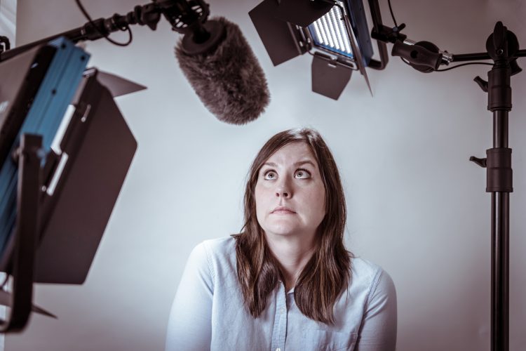 Woman surrounded by video and sound recording equipment, looking very nervous and trying to find the confidence to be on camera