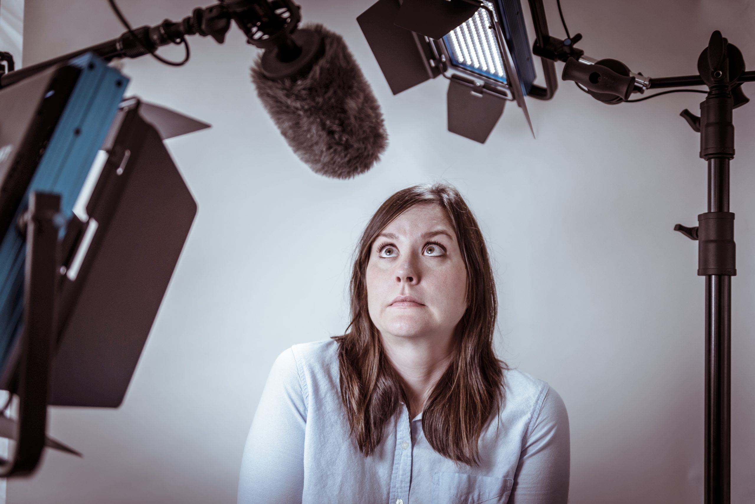 Woman surrounded by video and sound recording equipment, looking very nervous and trying to find the confidence to be on camera